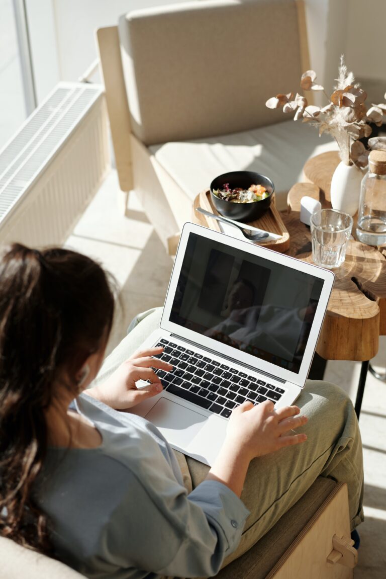 Woman sitting at a desk next to a window with sunlight working on a laptop with white decor