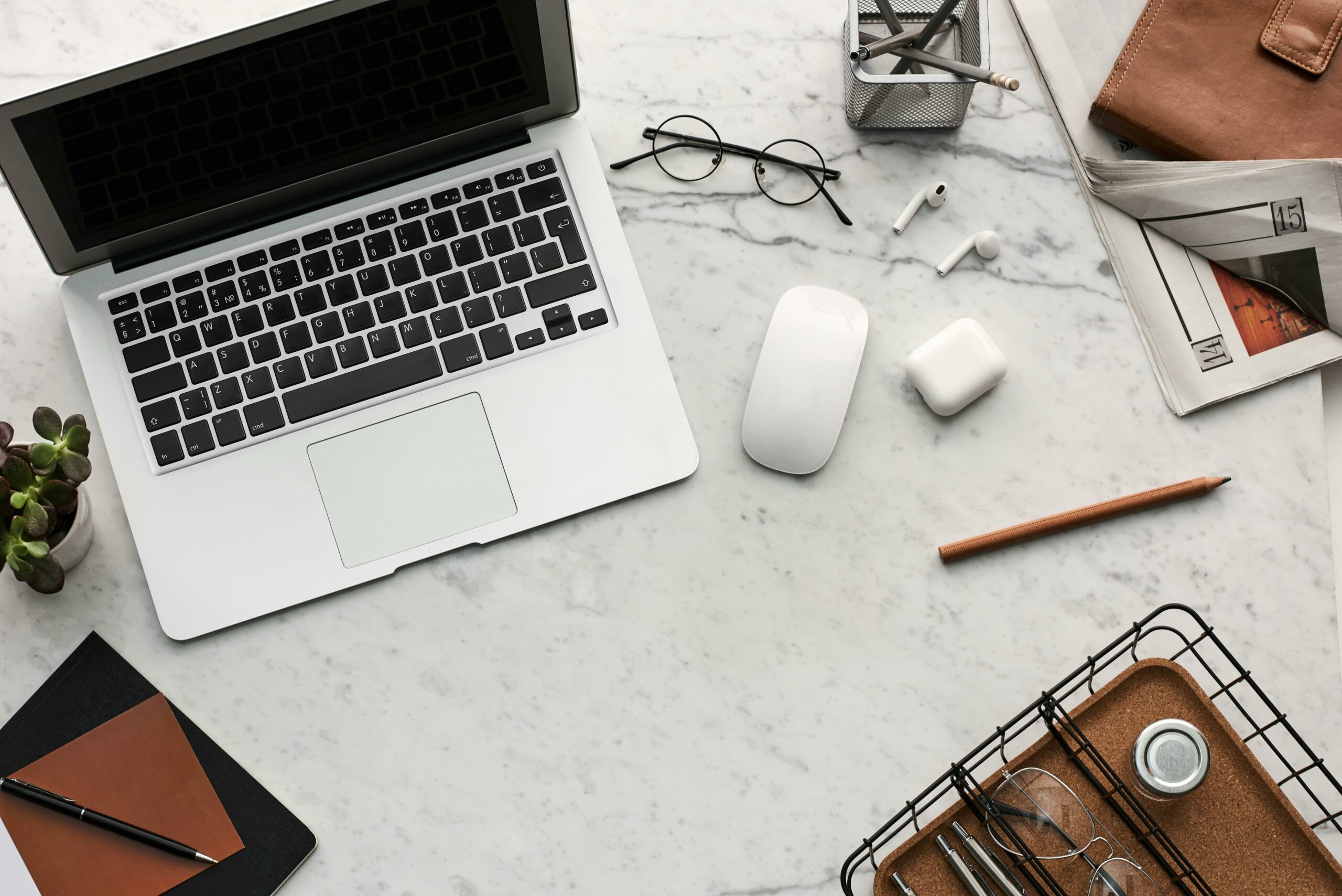 Macbook Laptop on a white table with glasses, wireless mouse, pencil, and other office items